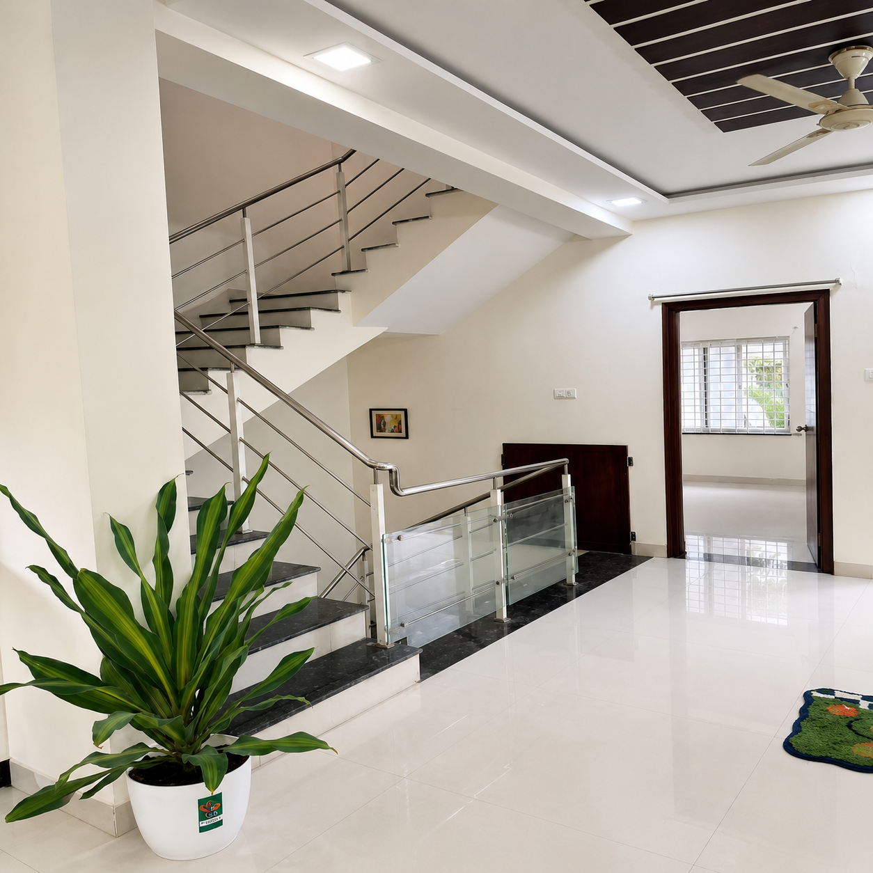 Modern staircase, contemporary staircase, stylish staircase, staircase interior, elegant staircase design, indoor staircase, residential staircase, duplex home staircase, apartment staircase, modern home interior, spacious hallway, bright hallway, clean interior, white tiled floor, glossy flooring, stainless steel railing, glass railing, modern handrail, staircase safety railing, black granite steps, granite staircase, floating-style staircase, open staircase design, minimalist staircase, modern landing area, indoor plants, potted plant, decorative greenery, natural home decor, bright lighting, LED ceiling lights, false ceiling, decorative ceiling, ceiling fan, spacious living area, clean home entrance, organized home, functional interior, urban home design, contemporary house interior, student-friendly home, student accommodation, student living space, convenient staircase access, business professional accommodation, professional-friendly home, comfortable living environment, work-life balance space, modern rental property, practical home layout, real estate interior.